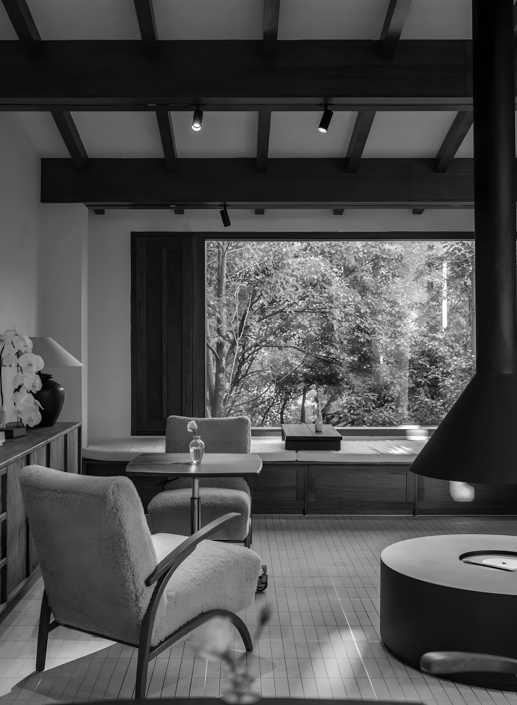 A quiet room with a hanging fireplace, armchairs and a window onto trees
